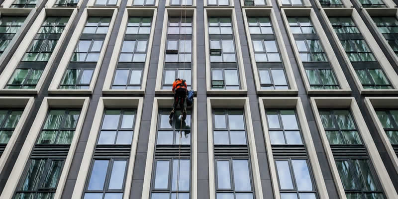 Technician midway up a high-rise building, surrounded by window reflections