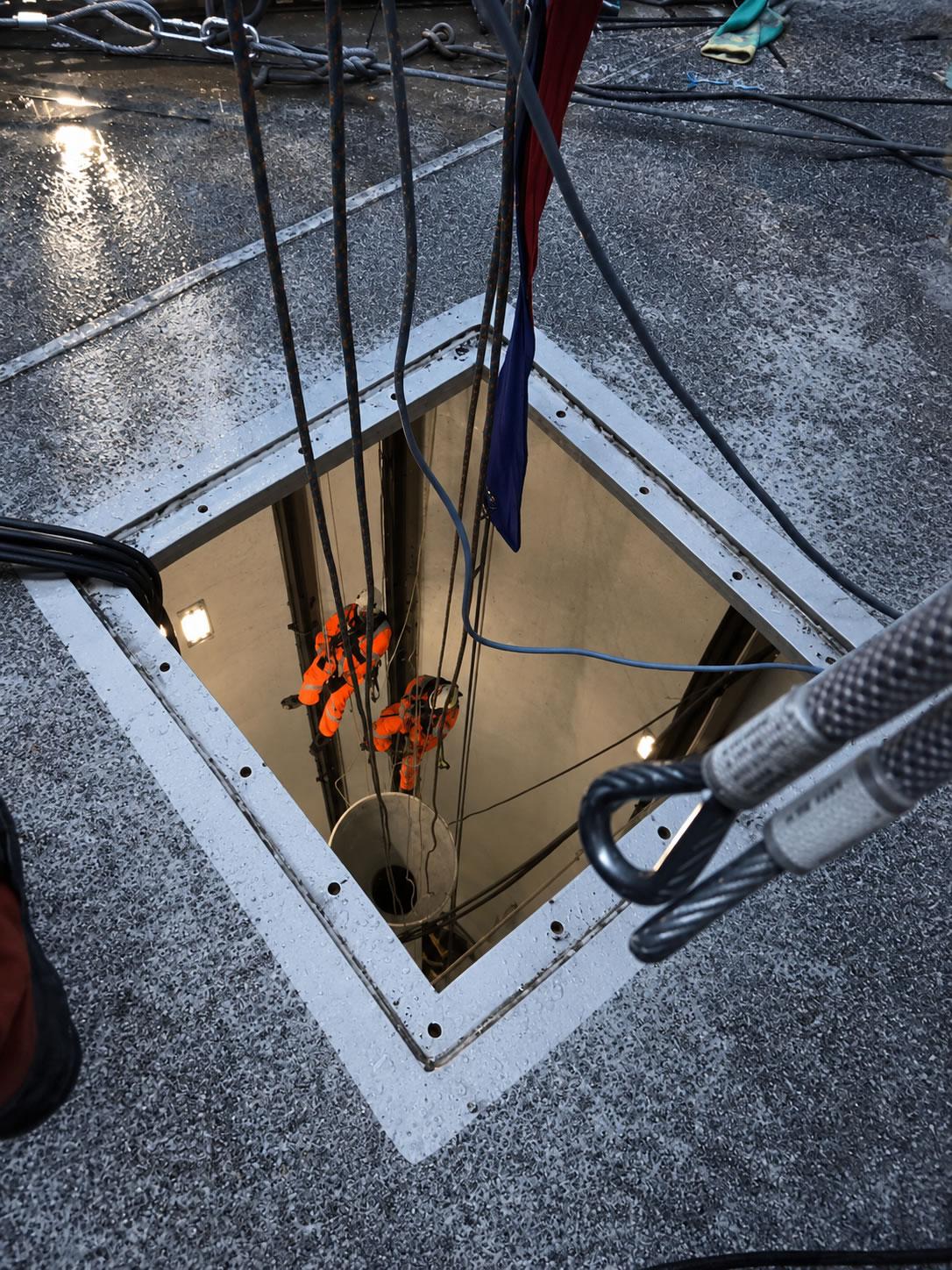 Technicians working inside the structure, viewed through a topside access opening