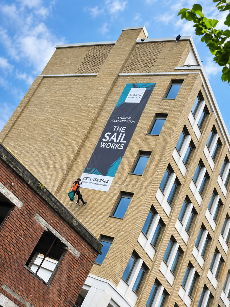 View down from the rope access position towards a technician and the roof of the building below