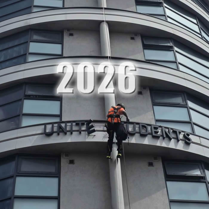 Technician installing large building signage at height on a student accommodation building
